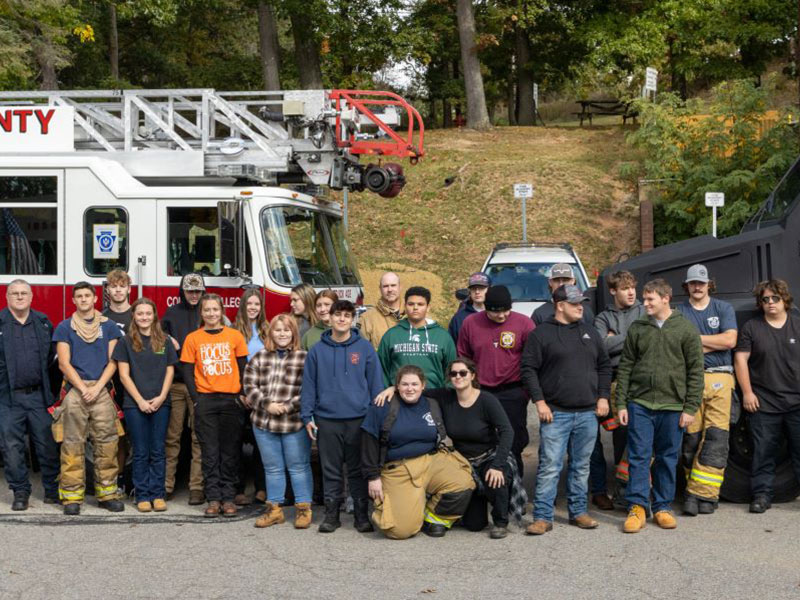 Students in CCAC’s Vocational Education Training program pose with first responders in front of a firetruck and SWAT vehicles.