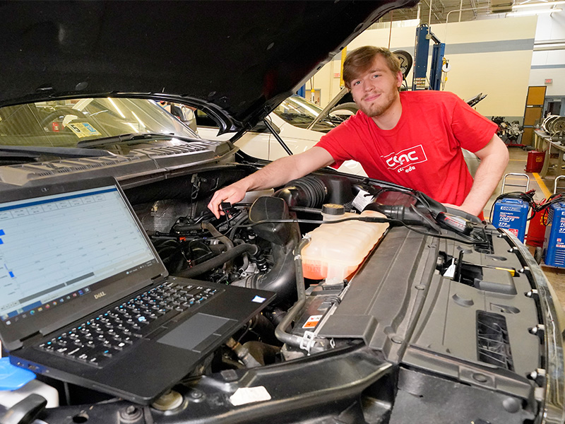 A student uses a laptop to run engine diagnostics under a vehicle's hood at CCAC's West Hills Center. 
