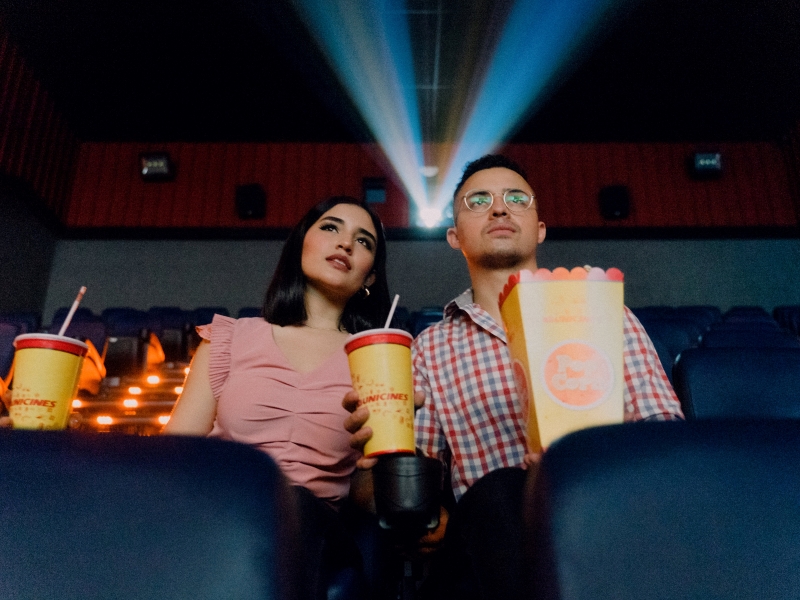 A man and woman sit in a movie theater, framed by the light of the film projector.