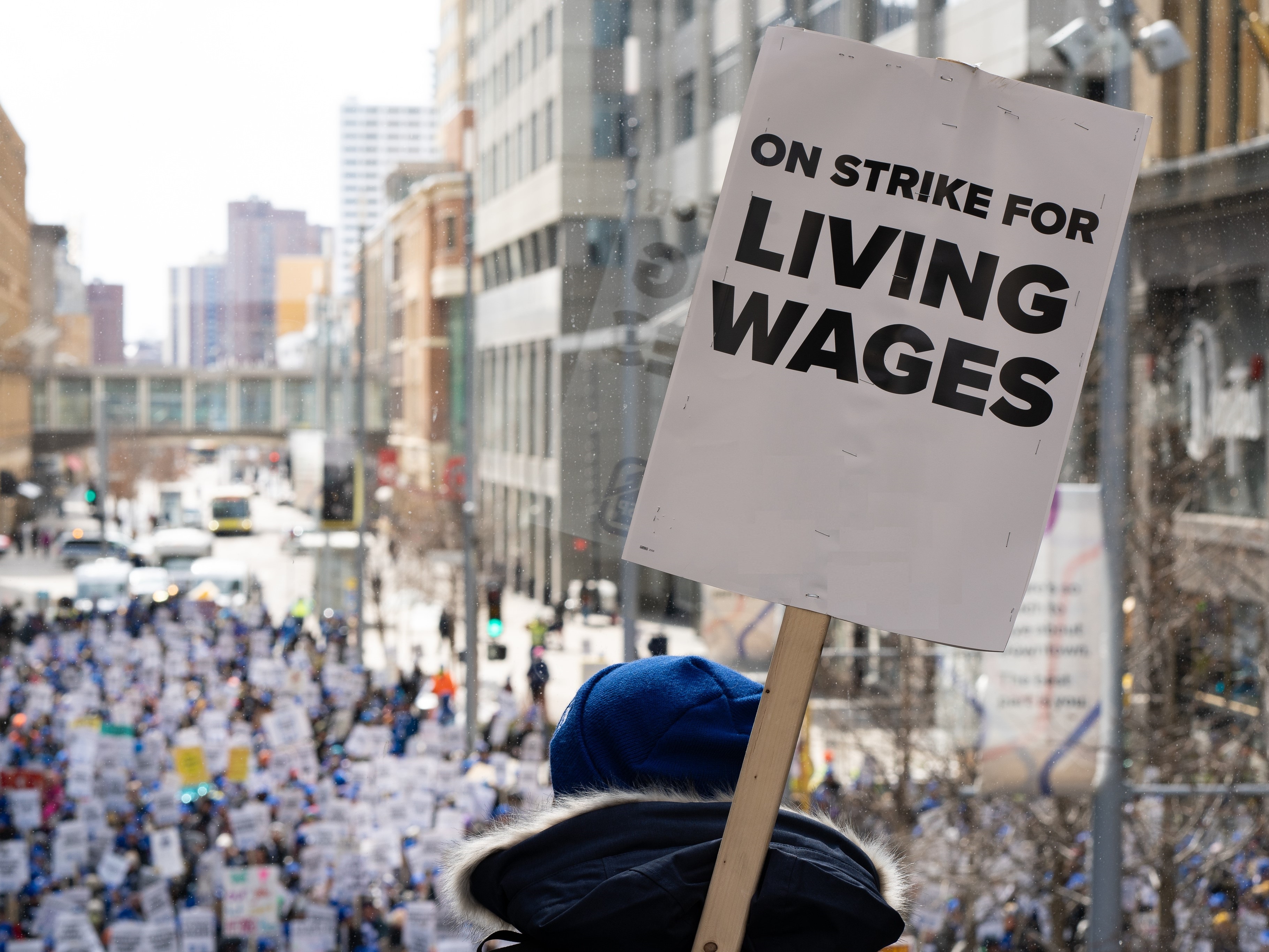 Workers march down a city street holding signs that read “ON STRIKE FOR LIVING WAGES.” 