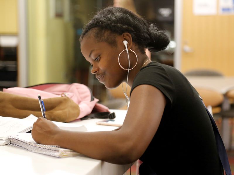 A CCAC student smiles slightly as she writes in a notebook.