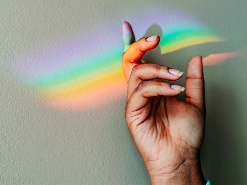 Rainbow light from a prism illuminates someone’s hand against a white wall.