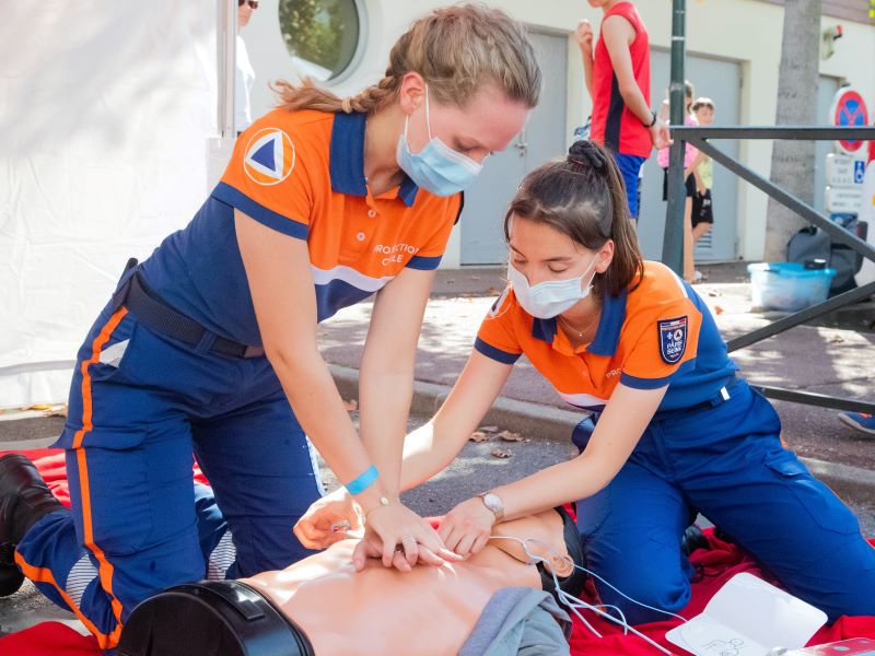 Two women in EMT uniforms practice CPR techniques on a dummy.