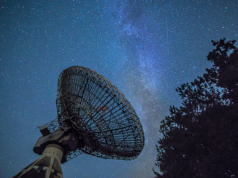 A large parabolic antenna points toward the starry night sky.