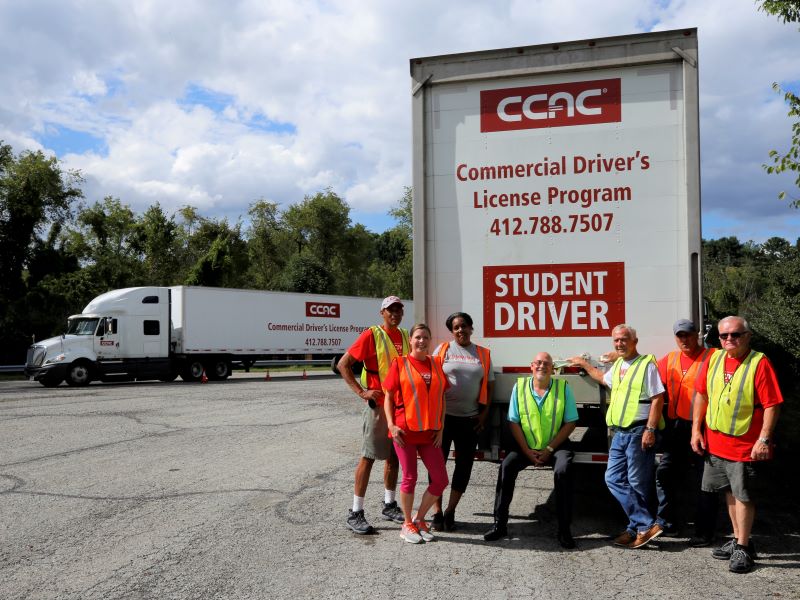 CCAC students and instructors wear neon safety vests as they smile alongside the college’s semi-trailer trucks.