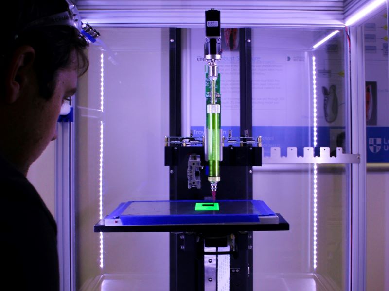 A man watches as an industrial 3D printer begins constructing an object.