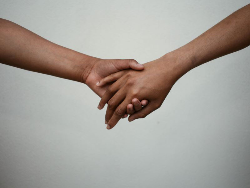 Two arms reach across empty space to hold hands affectionately.