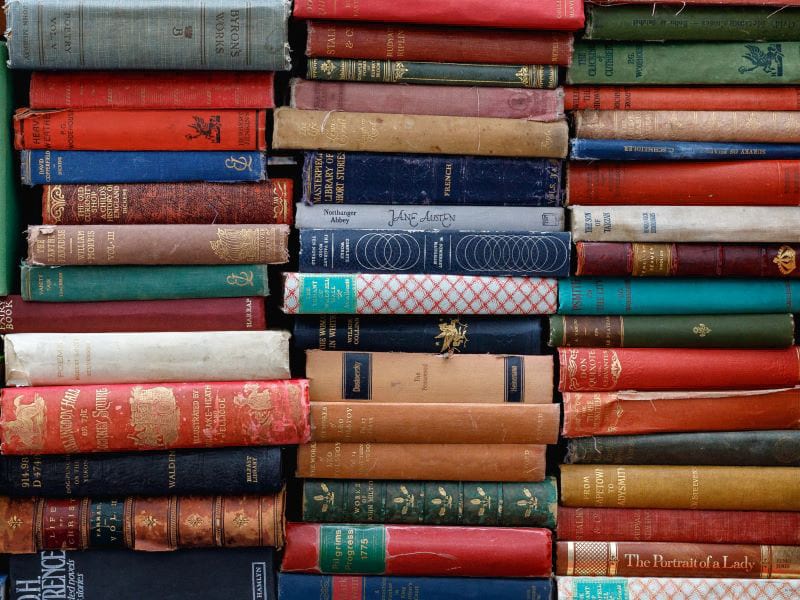 Dozens of colorful books are tightly stacked one on top of the other in three piles standing side by side.
