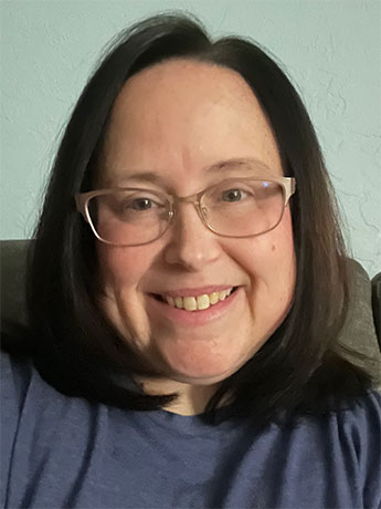 A white woman with shoulder length, straight black hair wearing glasses and smiling.